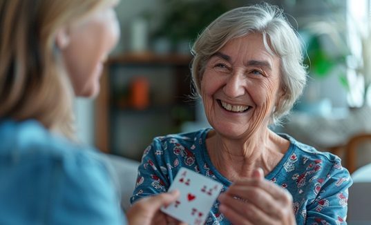 Betreuungskraft und Senior beim Kartenspiel – gelungene Integration im Haushalt